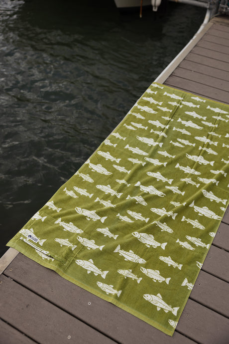 Green towel with fish pattern on a wooden dock by water