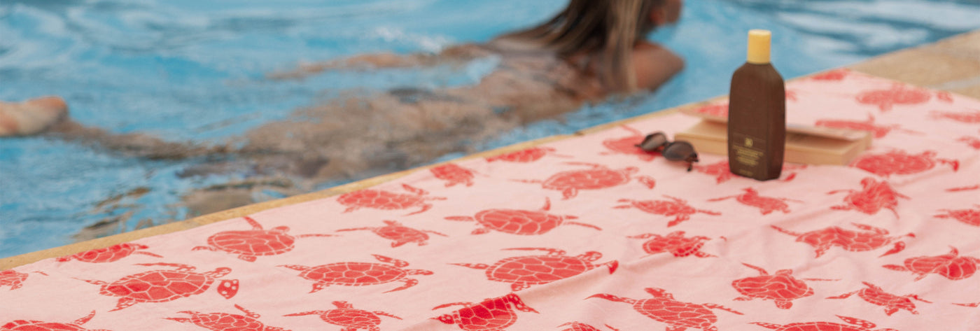 Pink sea turtle patterned towel poolside with swimmer in background