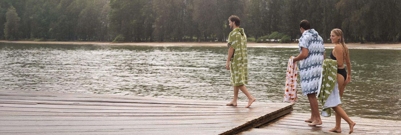 Three people on a dock with fish, wave, and sun-print towels and ponchos.