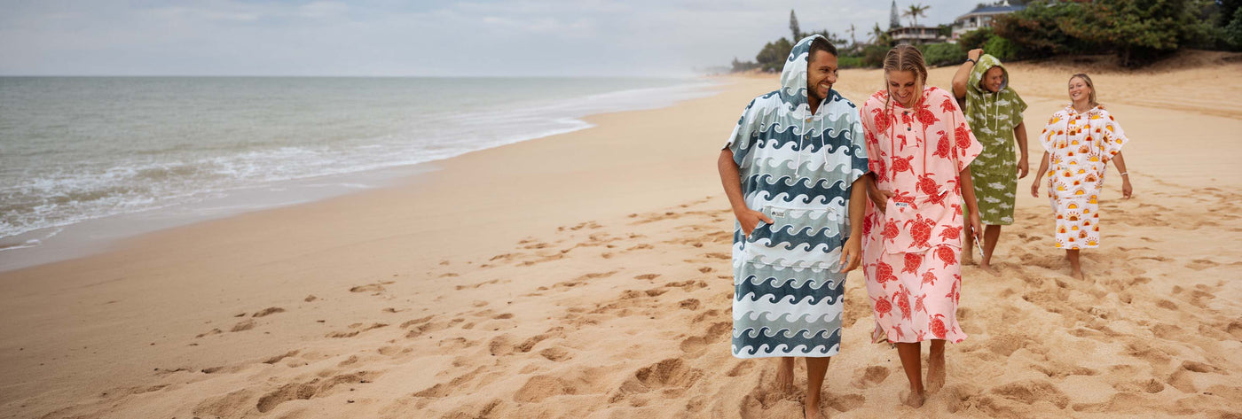 Four people walking on a beach wearing colorful towel ponchos