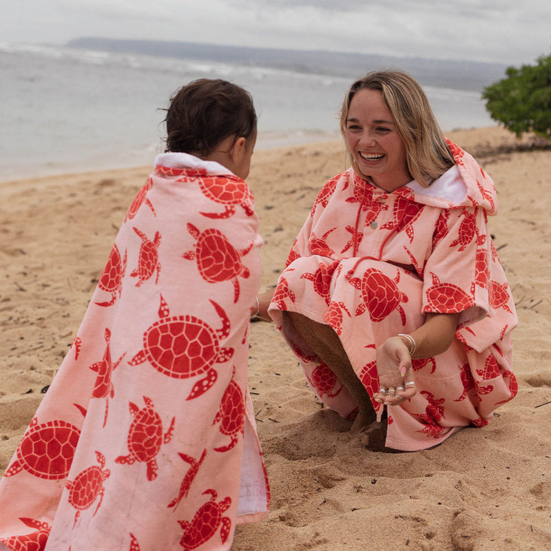 Woman and child on a beach wearing matching pink turtle patterned towels.