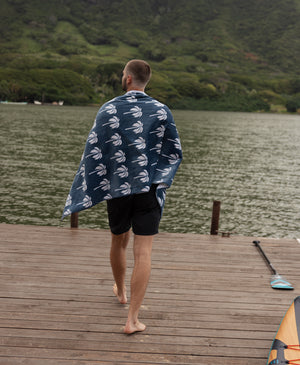 Man walking on a dock with a towel draped over his shoulders, surrounded by a natural landscape.