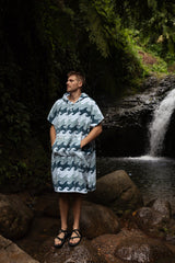 Person wearing a blue wave-patterned poncho standing in front of a waterfall.