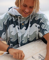 Close up of a person wearing a wave-patterned towel poncho prepping a surfboard.