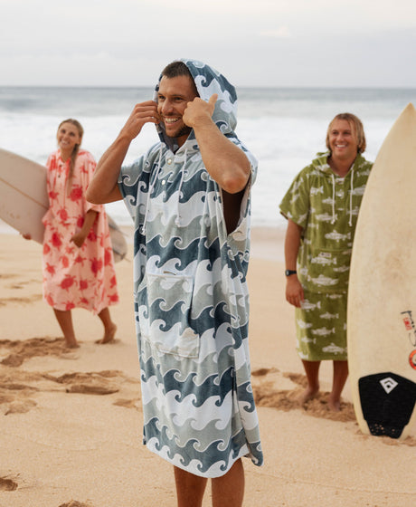 Man on a beach in a wave-print towel poncho with surfers in the background.