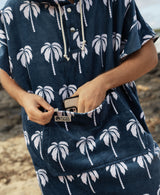Person wearing a navy blue towel poncho with white palm tree pattern, putting a phone in zipper pocket