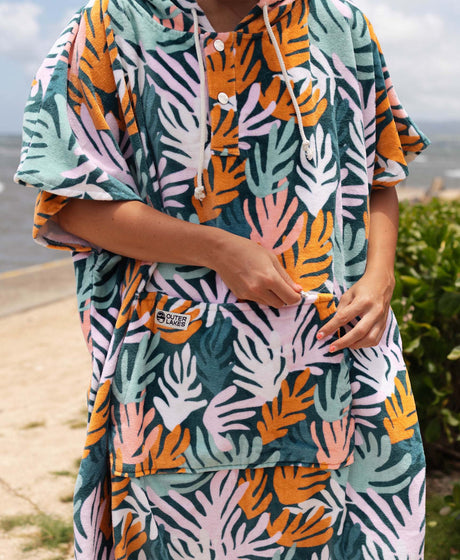 Person wearing a colorful tropical patterned towel poncho with a beach background