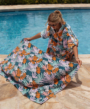 Person laying out a colorful coral patterned towel by a pool.