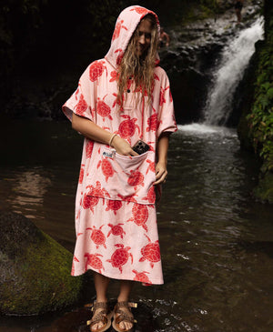 Woman in a pink turtle-print towel poncho standing in front of a waterfall.