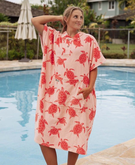Woman wearing a pink turtle patterned towel poncho by a pool.