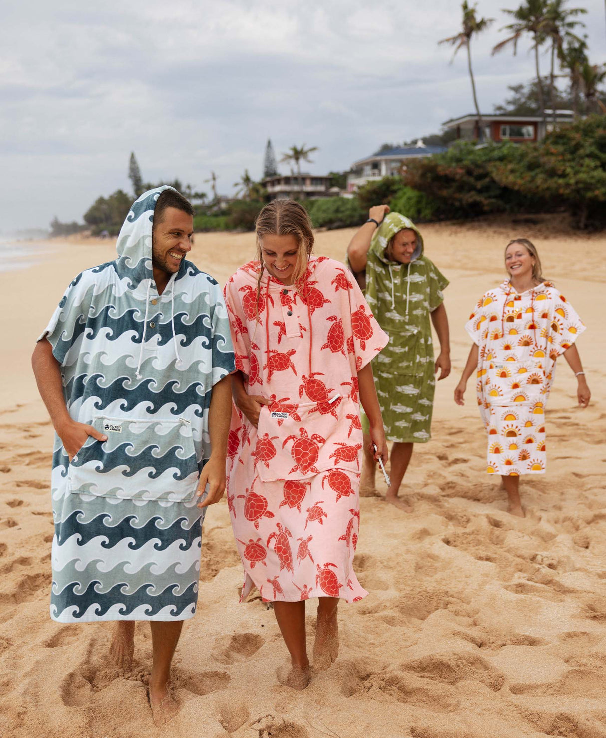 Four people on a beach wearing colorful hooded towel ponchos.
