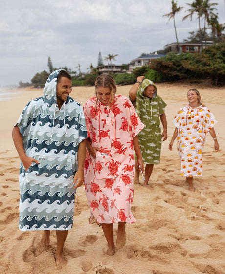 Four people on a beach wearing colorful hooded towel ponchos.