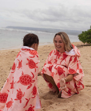 Woman and child on a beach wearing matching pink turtle patterned towels. 