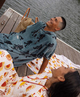 Two people laughing on a dock, one in Bigfoot-print poncho, one in sun-print poncho.