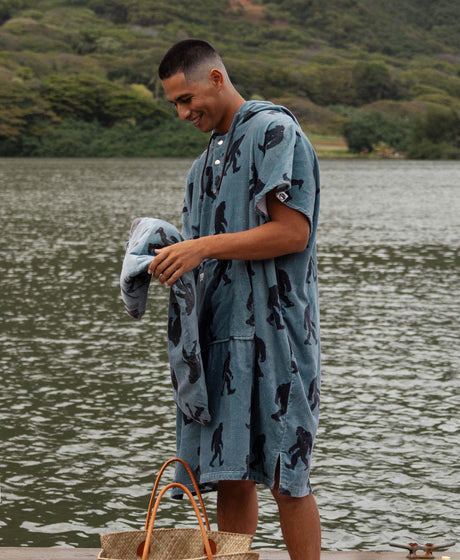 Man wearing a blue and grey bigfoot patterned towel poncho by a body of water
