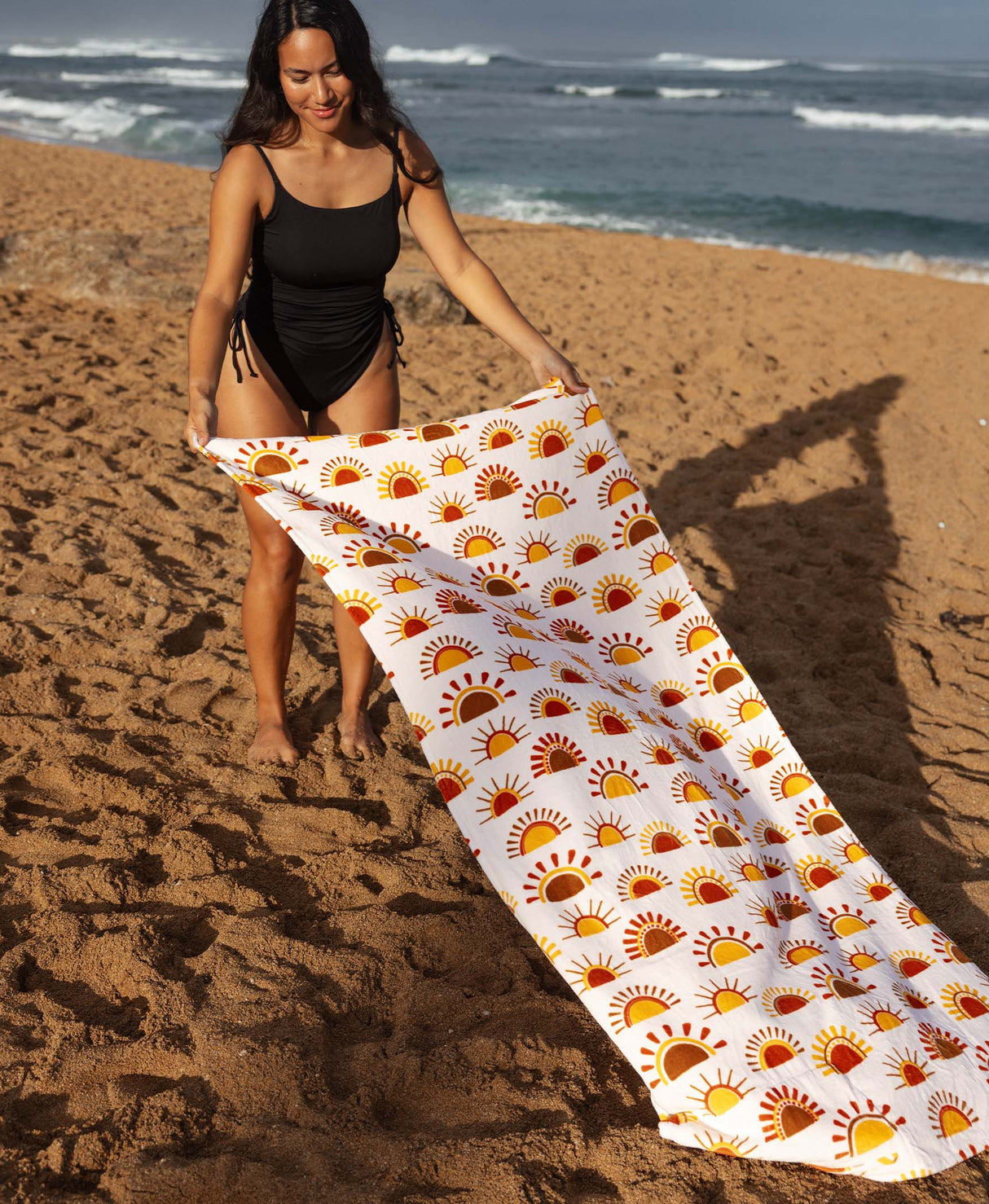 Woman on a beach holding a sun-patterned towel