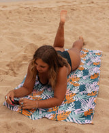 Woman lying on a colorful coral patterned beach towel on a beach