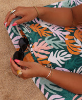 Person putting sunglasses into zipper pocket that's on a coral patterned beach towel.