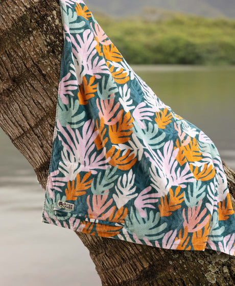 Colorful  coral patterned towel draped over a palm tree with a blurred natural background