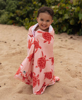 Child wrapped in a pink turtle towel on a sandy beach.