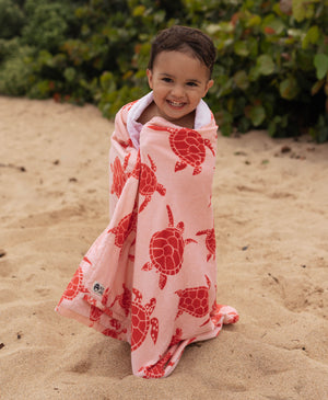 Child wrapped in a pink turtle towel on a sandy beach.