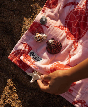 Pink turtle-print towel with shells on it, hand placing starfish in the pocket.