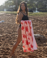 Woman holding a pink turtle patterned towel on a sandy beach