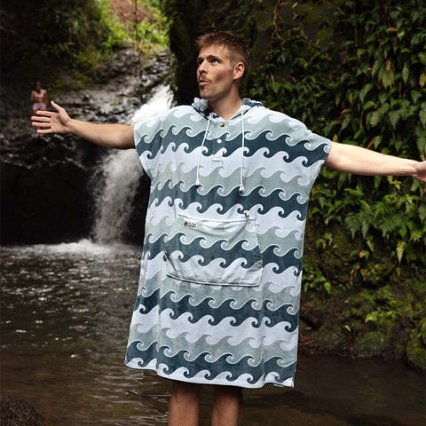 Man wearing a blue wave-patterned towel poncho standing by a waterfall