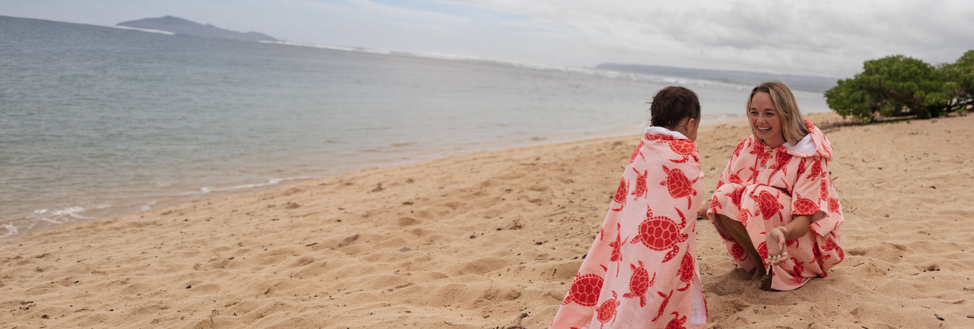 Woman and child sitting on a beach wearing matching pink turtle patterned towels